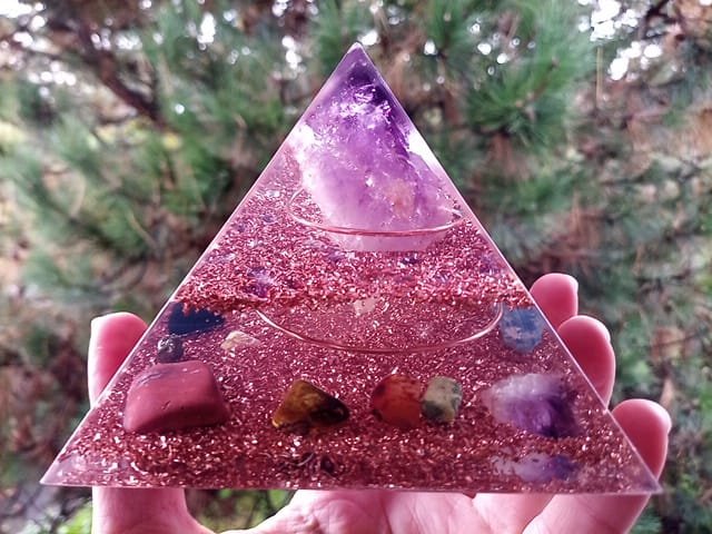 Amethyst orgone pyramid with red jasper, carnelian and tigers eye crystals in front of tree.