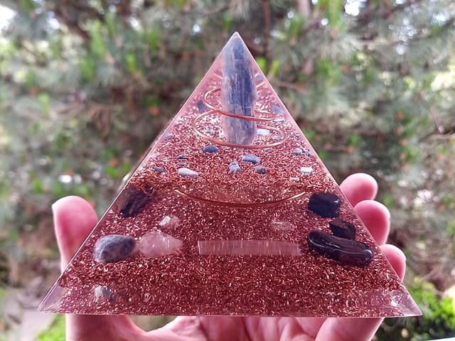 Blue kyanite orgone pyramid energy generator with selenite crystal in front of tree.