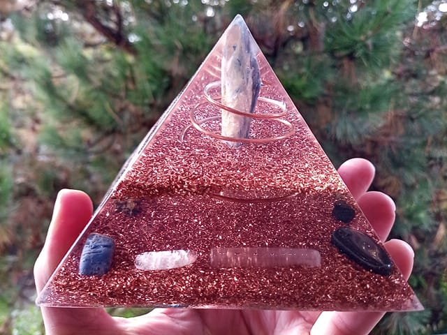 Blue kyanite orgone pyramid with rose quartz and selenite in front of a tree.