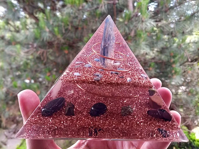 Blue Kyanite orgone pyramid with black tourmaline and shungite in front of a tree.