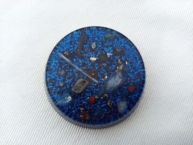 Blue orgone pocket disc with blue kyanite and amethyst crystals on a white cloth.