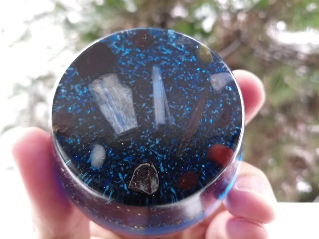 Blue orgone puck being held up in front of a tree.