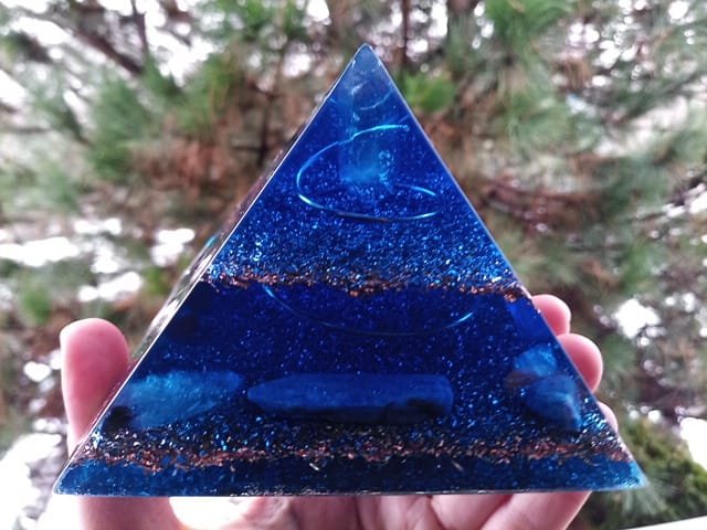 Blue orgone pyramid with blue kyanite blade and amethyst crystal inside, in front of a tree