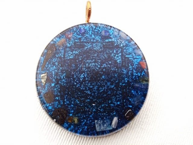 Blue Sri Yantra orgone pendant on a white cloth.