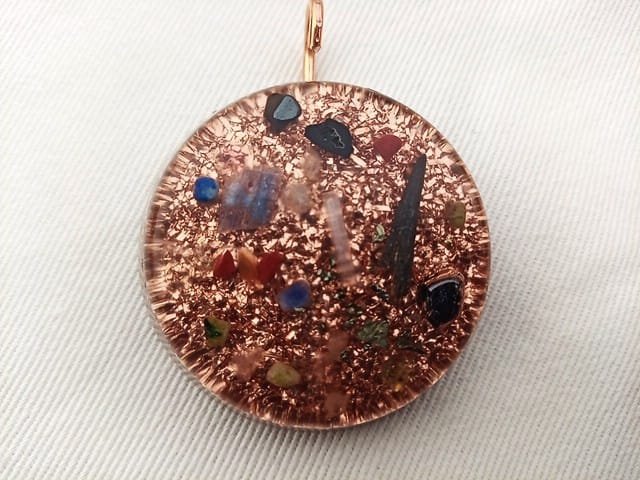 Clear orgone pendant with crystals on top of copper on a white cloth