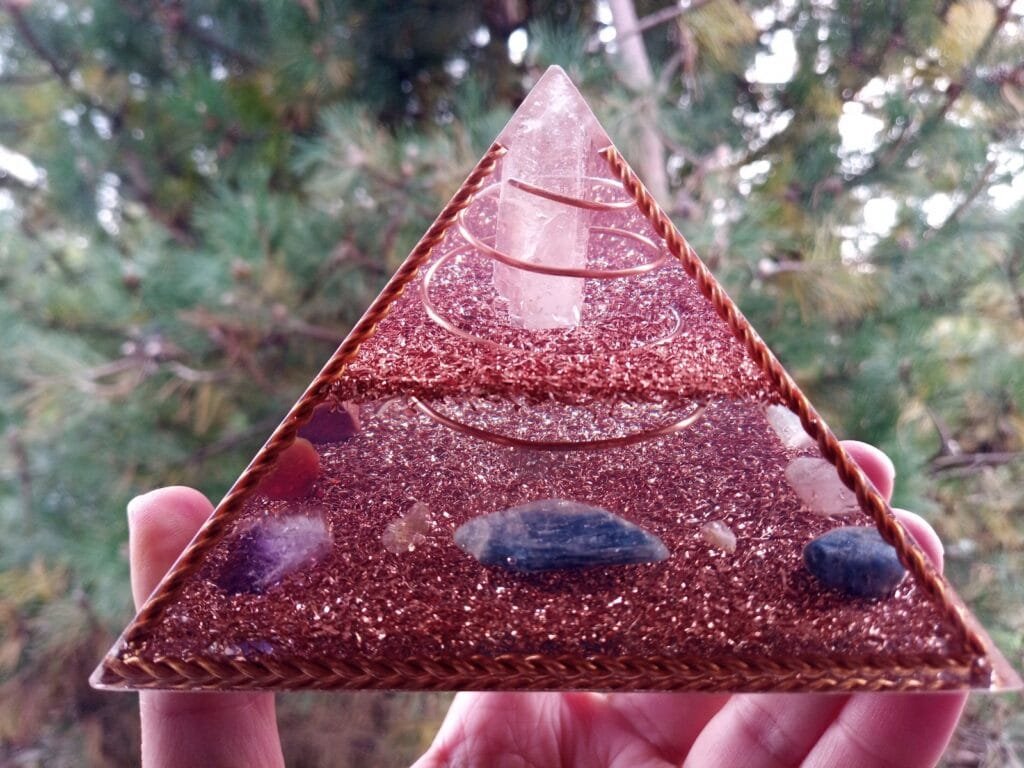 Copper Frame orgone pyramid being held in front of a pine tree.