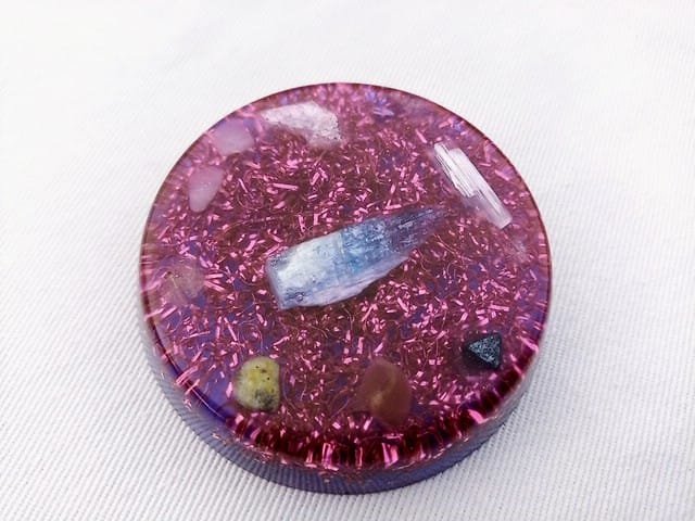 Violet Crown Chakra orgone disc with blue kyanite in the center on a white cloth.