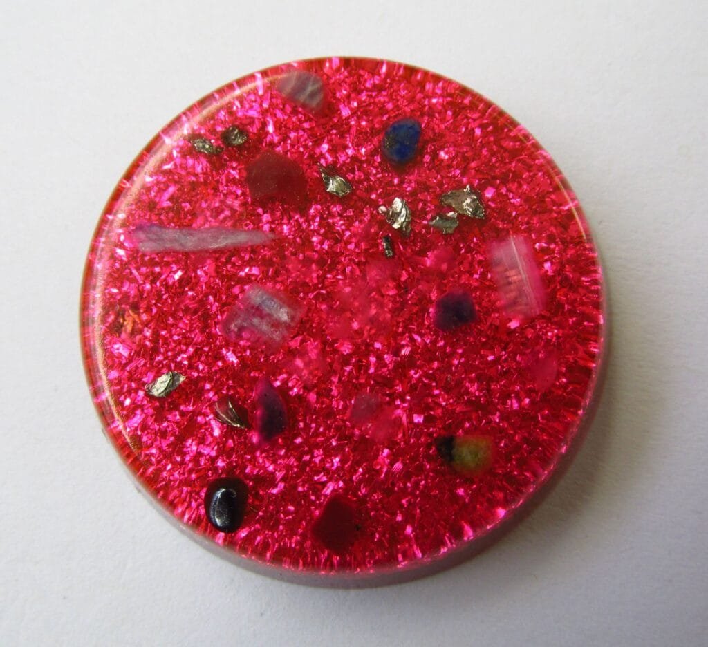 Pink Divine Love orgonite disc with blue kyanite and carnelian on a white background.