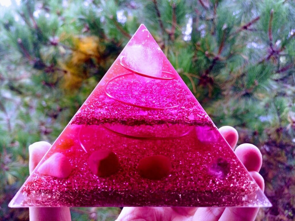 Divine Love orgonite pyramid with love crystals in front of a tree.