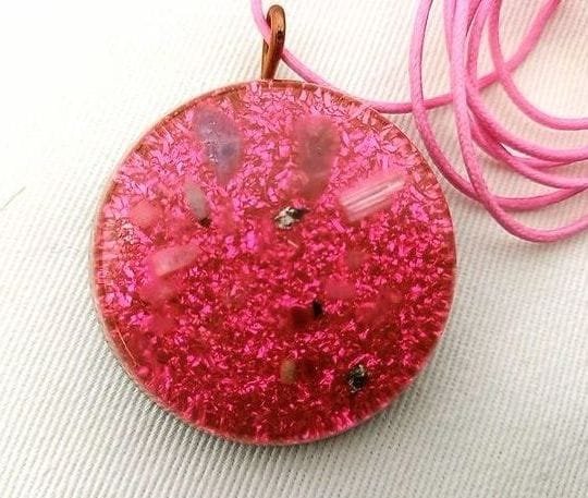 Pink divine love orgone pendant with selenite crystal and pink string on a white cloth