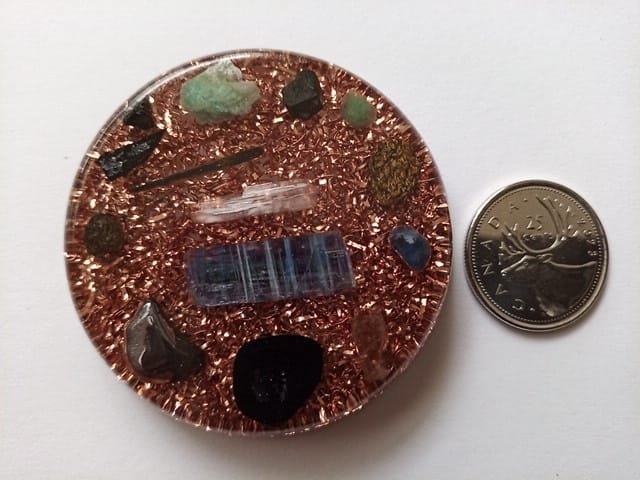 EMF orgone disc with a canadian quarter on a white cloth.