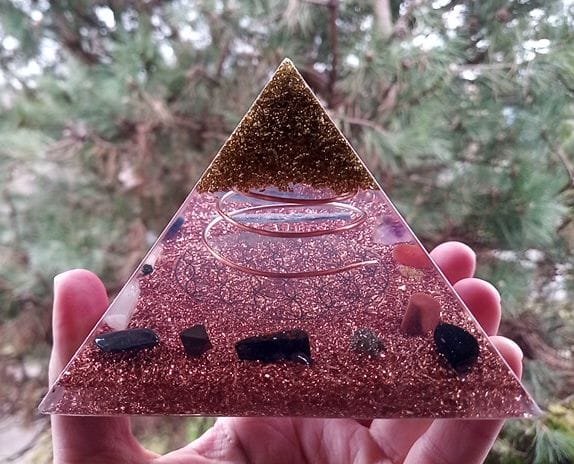 Flower of Life orgone energy pyramid being held in front of a tree.