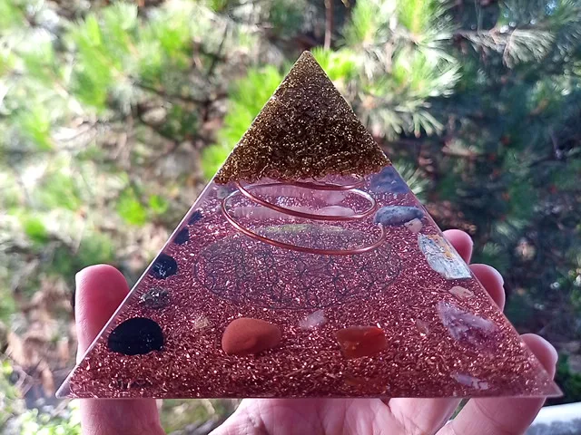 Flower of Life orgonite pyramid with brass on top, in front of a tree.