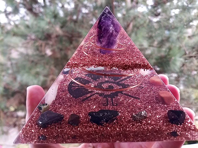 Galactic Butterfly orgone pyramid with amethyst point at the top, in front of a tree.