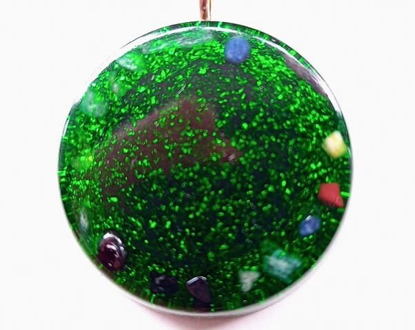 Green Flower of Life orgone pendant with healing crystals on a white background.