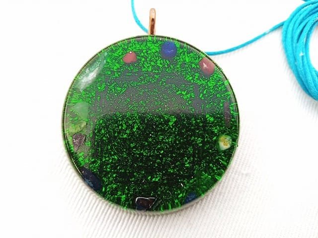 Green Sri Yantra orgone pendant with turquoise string on a white cloth.