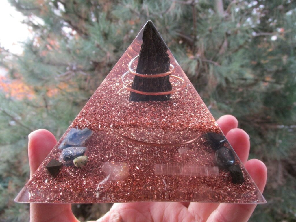 Grounding Orgone Pyramid with clear resin and copper in front of a pine tree.