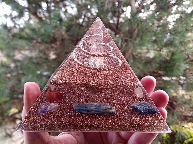 Lemurian Seed Crystal orgone pyramid being held in front of a pine tree.