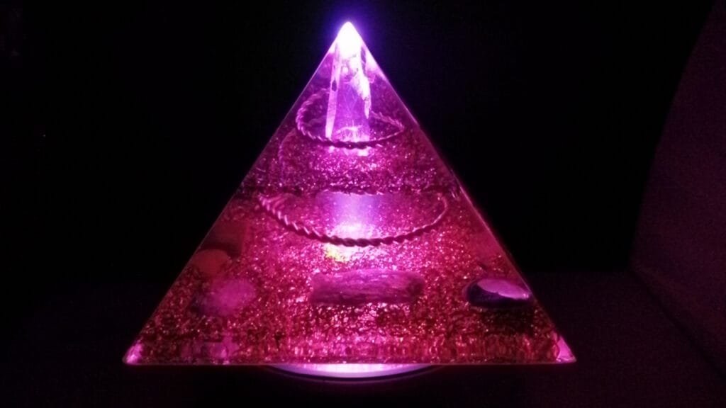 Lemurian Seed Crystal orgone pyramid glowing on top of an led light stand.