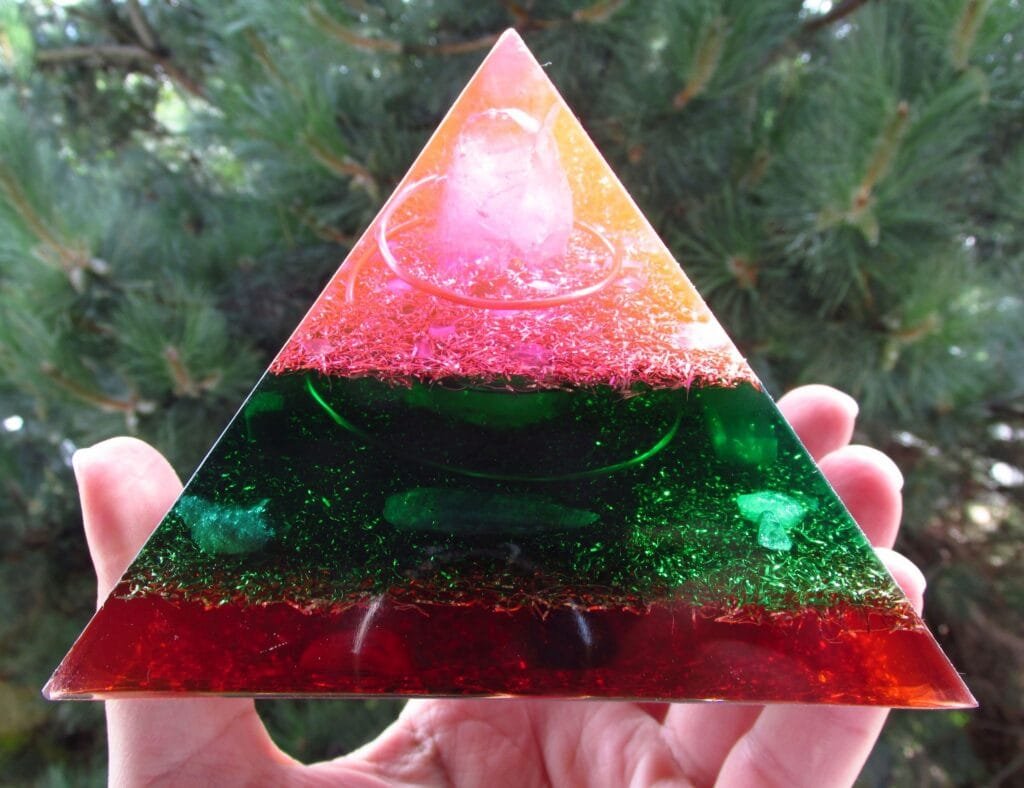 Love Soulmate orgonite Pyramid, pink, green and red, in front of a pine tree.