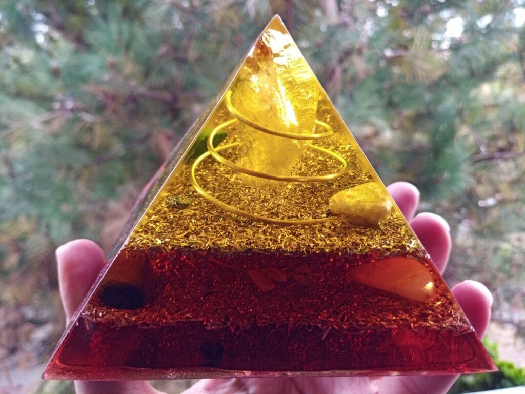 Lower Chakra orgone pyramid with citrine crystal at the top in front of a tree.