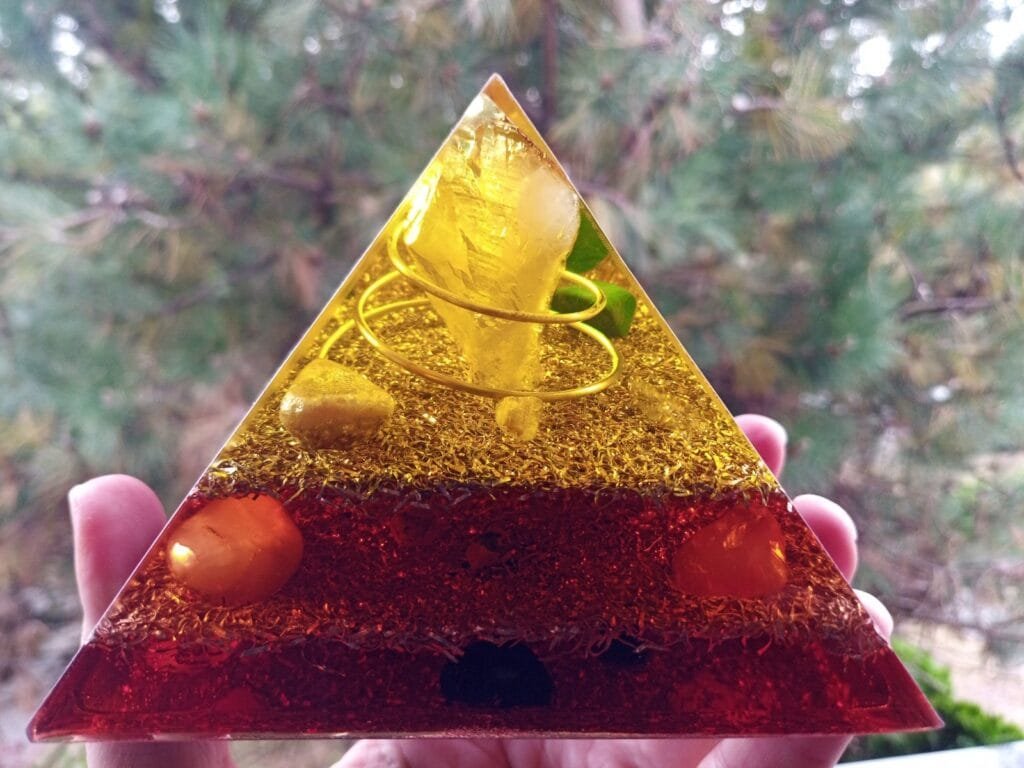 Lower Chakra orgone pyramid with citrine point, sunstone and carnelian, in front of pine tree.