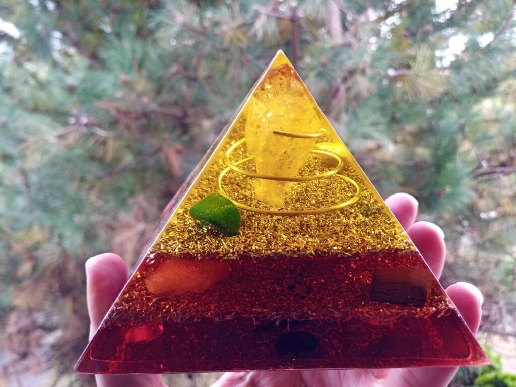 Lower Chakra orgone pyramid with citrine crystal being held in front of a tree.