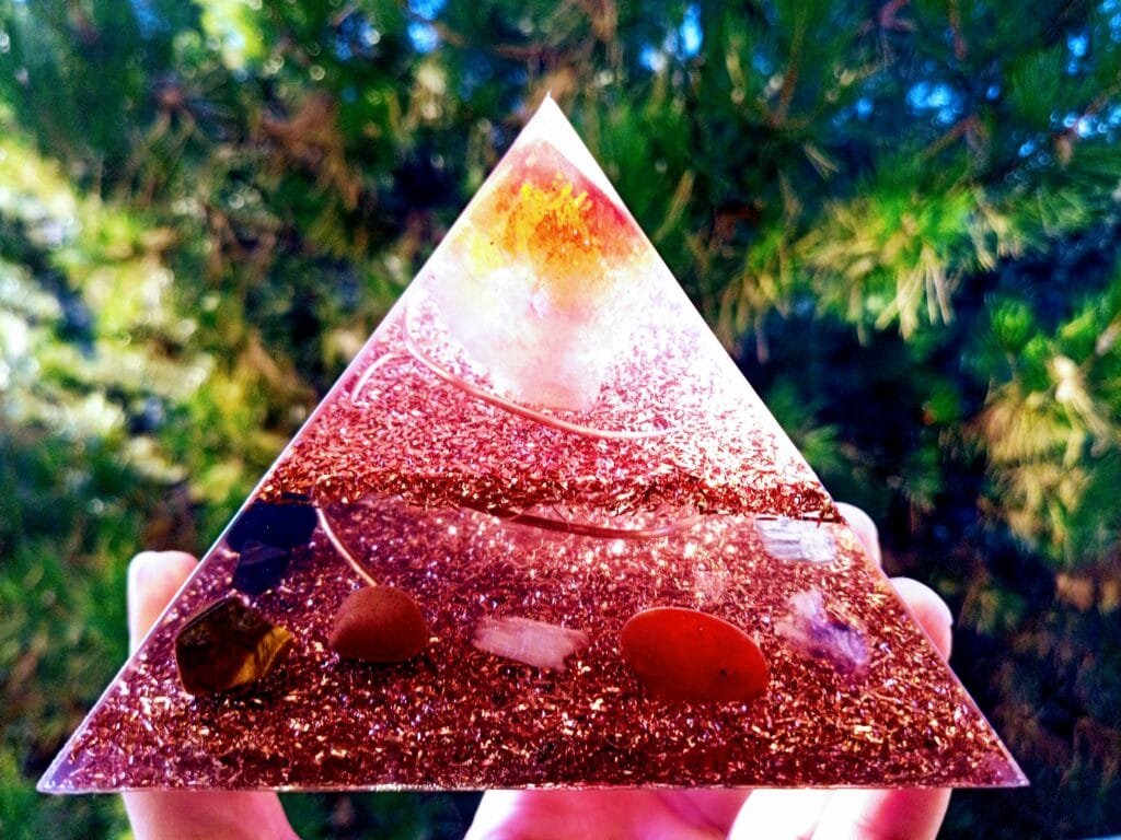 orgone energy pyramid, held in front of a tree with citrine, selenite, amethyst orgonite crystals