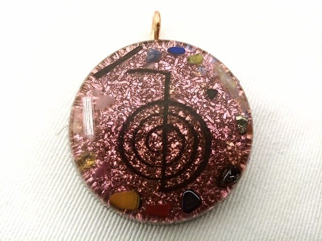 Violet reiki orgonite pendant with red jasper and carnelian crystals on a white cloth.