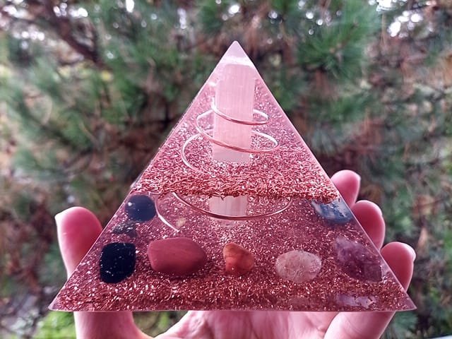 Selenite orgone pyramid, made of clear resin, copper and crystals, in front of tree.