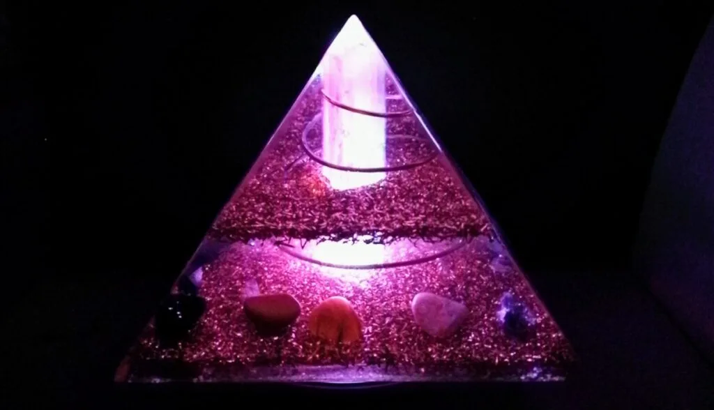 Selenite orgone pyramid, glowing, on top of an led light stand.