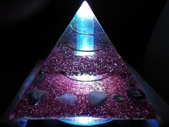 Selenite orgone pyramid glowing on top of an led light stand.