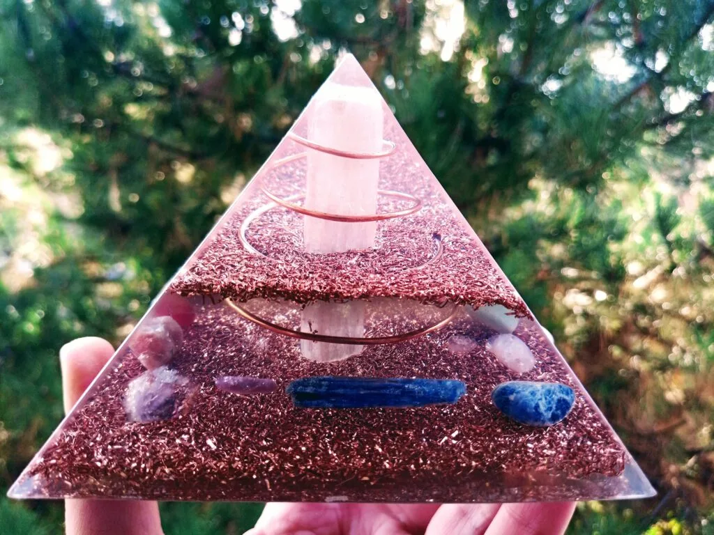 Selenite orgonite pyramid with selenite rod in center in front of a tree.