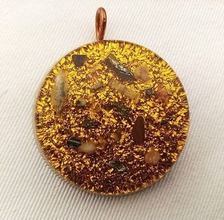 Yellow solar plexus chakra orgone pendant with clear quartz and citrine on white cloth.