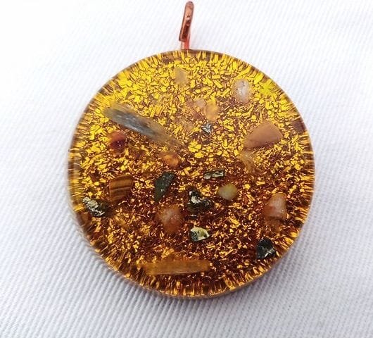 Yellow solar plexus chakra orgone pendant with with sunstone and tigers eye crystals on white cloth.