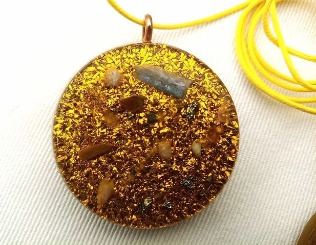 Yellow solar plexus chakra orgone pendant with chakra crystals with a yellow string on white cloth.