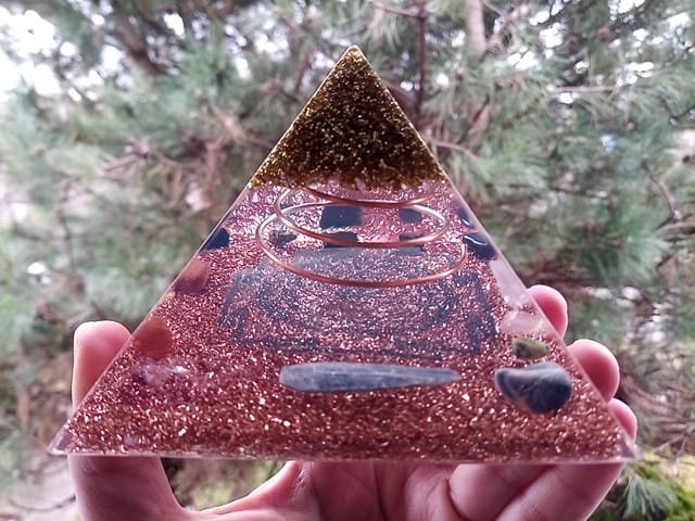 Sri Yantra Orgone Pyramid with blue kyanite and blue sodalite crystals in front of tree.