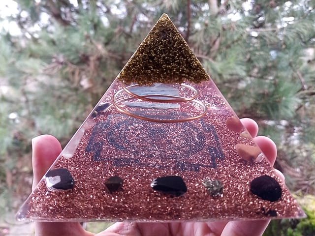 Sri Yantra Orgone Pyramid with black tourmaline and shungite in front of tree.