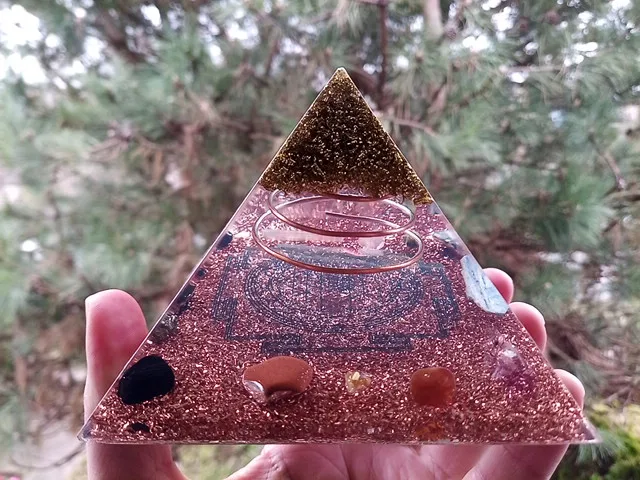 Sri Yantra Orgonite pyramid with brass on top held in front of a tree.