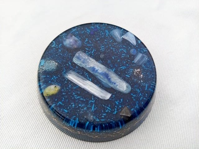 Blue throat chakra orgone disc on a white cloth.