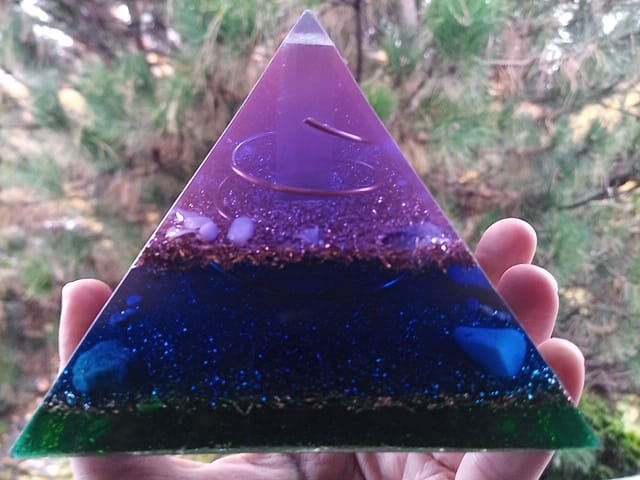 Upper Chakra Orgone Pyramid with selenite rod in the center, in front of a tree.