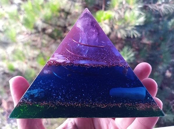 Upper Chakra Orgone Pyramid with chakra crystals in front of a tree.