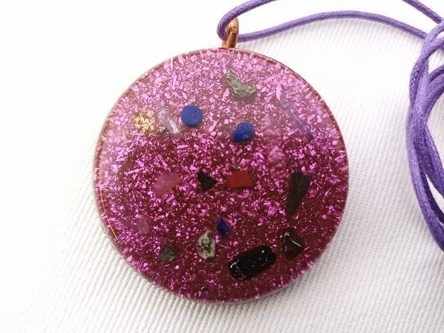 Violet orgone pendant with crystals and a violet string on white cloth