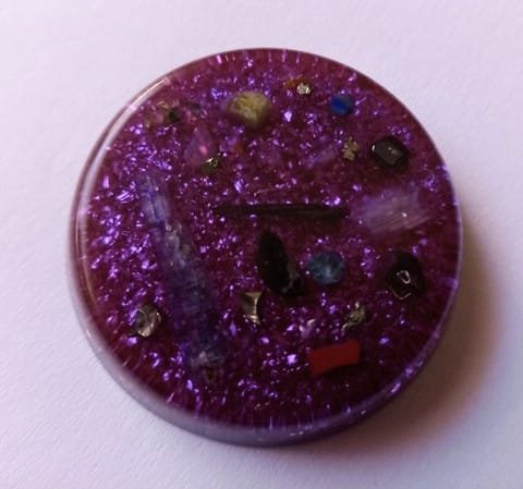 Violet orgone pocket disc with blue kyanite and amethyst crystals on a white cloth.