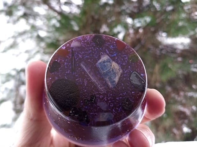 Violet orgone puck being held up in front of a tree.