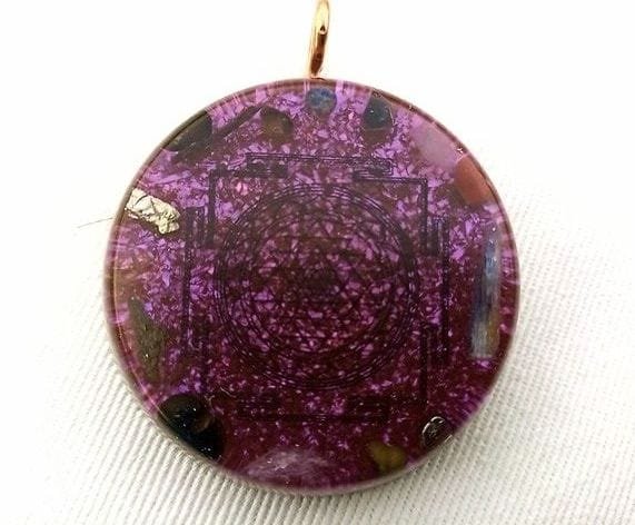 Violet Sri Yantra orgone pendant on a white cloth.