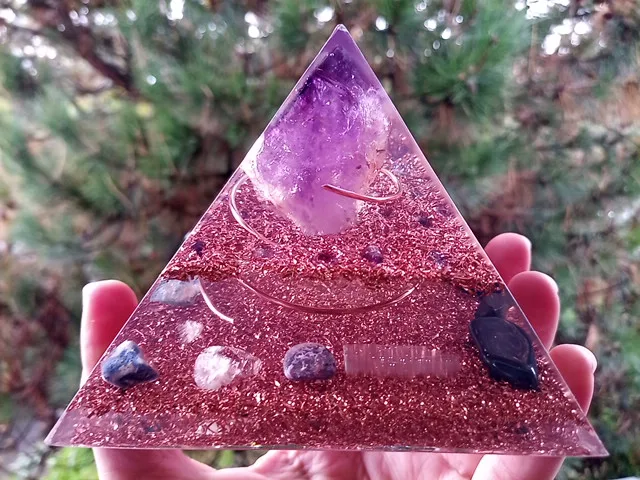 Amethyst orgone pyramid with selenite and rose quartz crystals in front of tree.