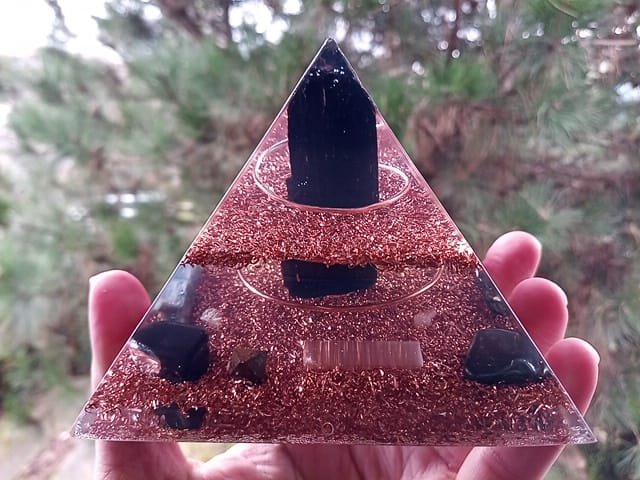 EMF orgone pyramid being held in front of a pine tree.