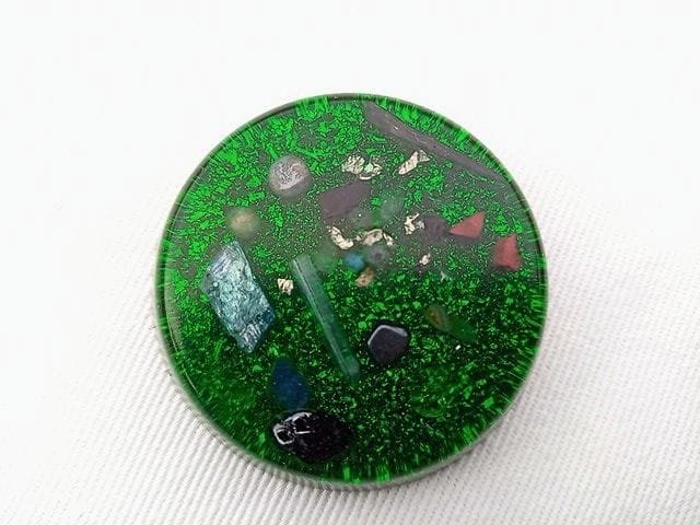 Green orgone pocket disc with blue kyanite and amethyst crystals on a white cloth.
