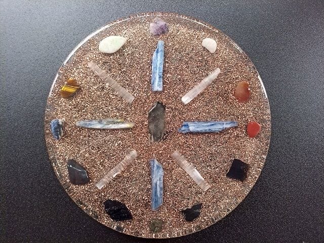 Clear orgone plate with copper underneath the crystals on a black table.